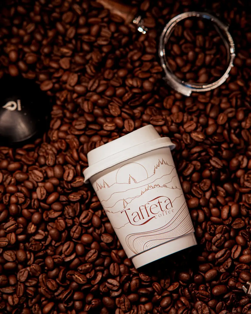 A Taffeta takeaway cup lying on a bed of roasted coffee beans
