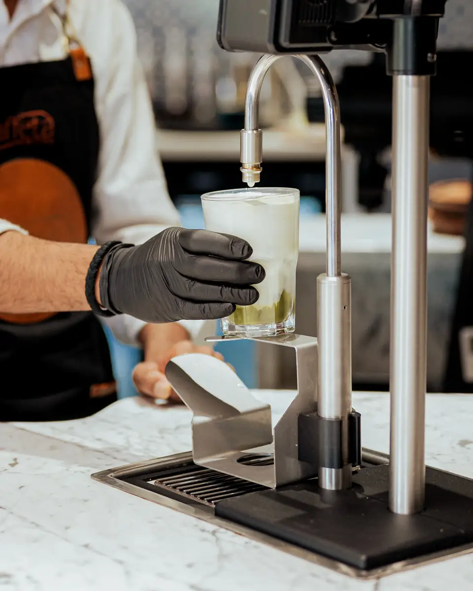 A gloved hand holding a glass under a chrome tap at the bar