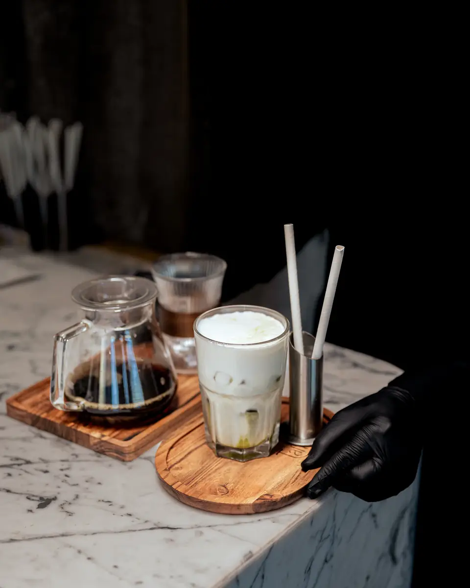 An iced latte, a carafe of coffee and a glass of espresso on wooden boards