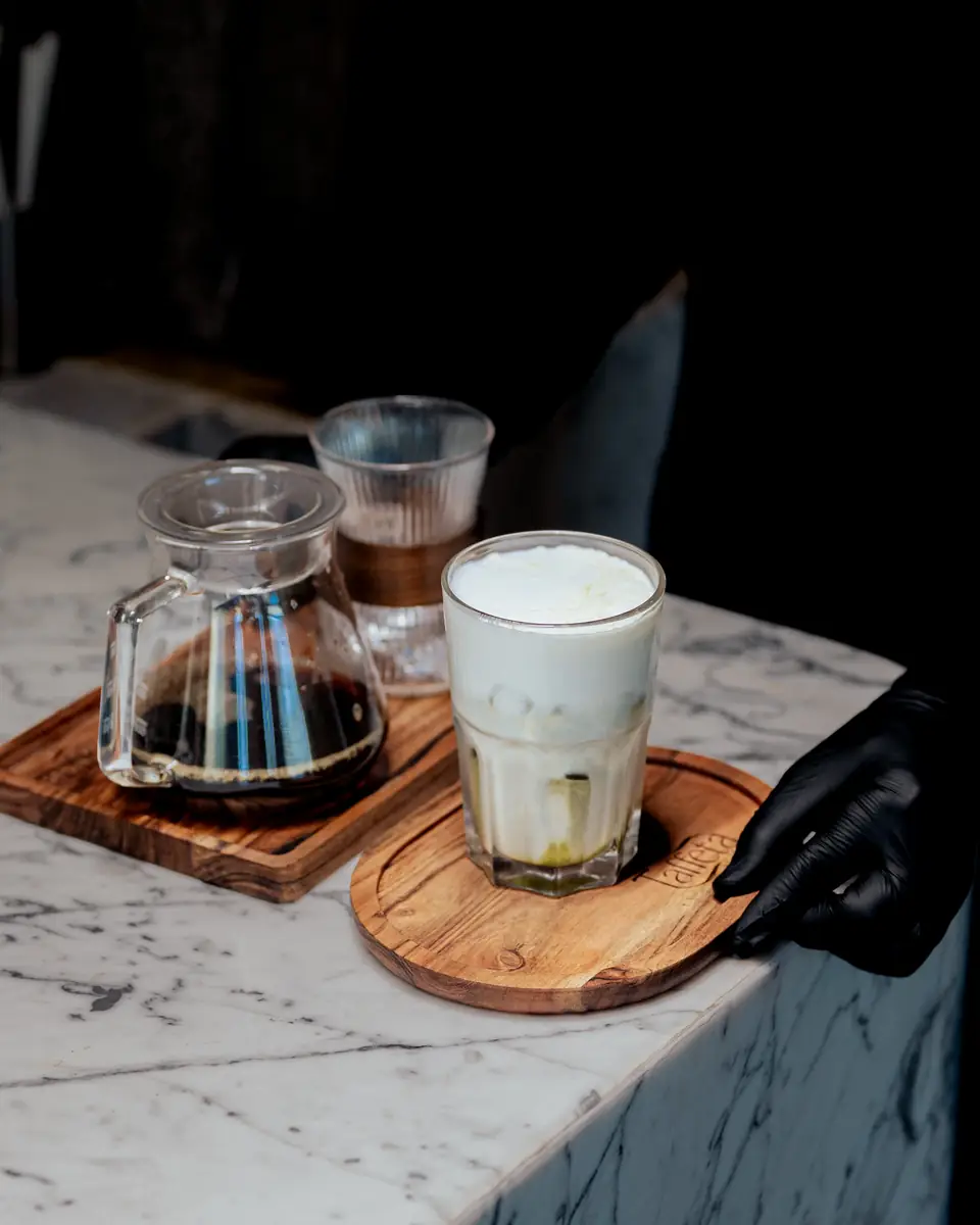 An iced latte and a carafe of brewed coffee served on wooden boards