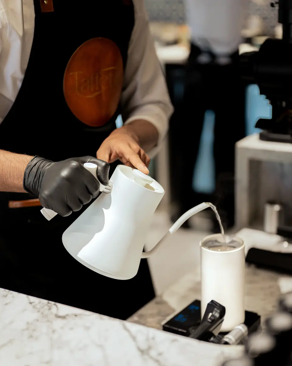 Close-up of a barista pouring from a white gooseneck kettle