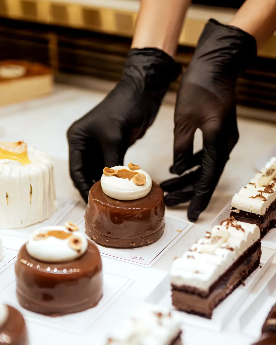 Gloved hands arranging chocolate entremets and cake bars on the counter
