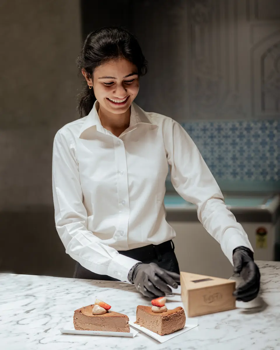A smiling team member boxing slices of cake at the marble counter