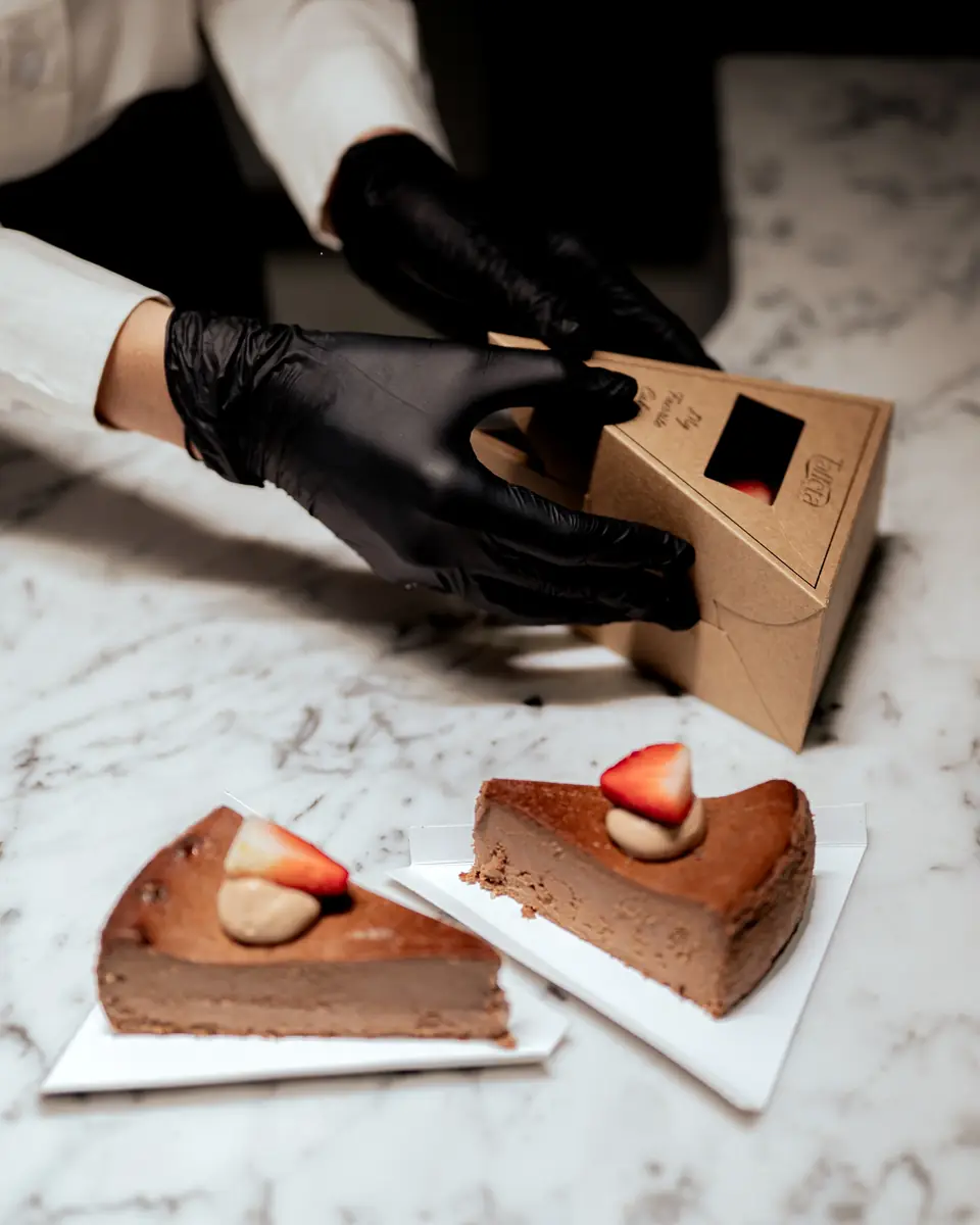 Gloved hands folding a cake box beside two slices of chocolate cake