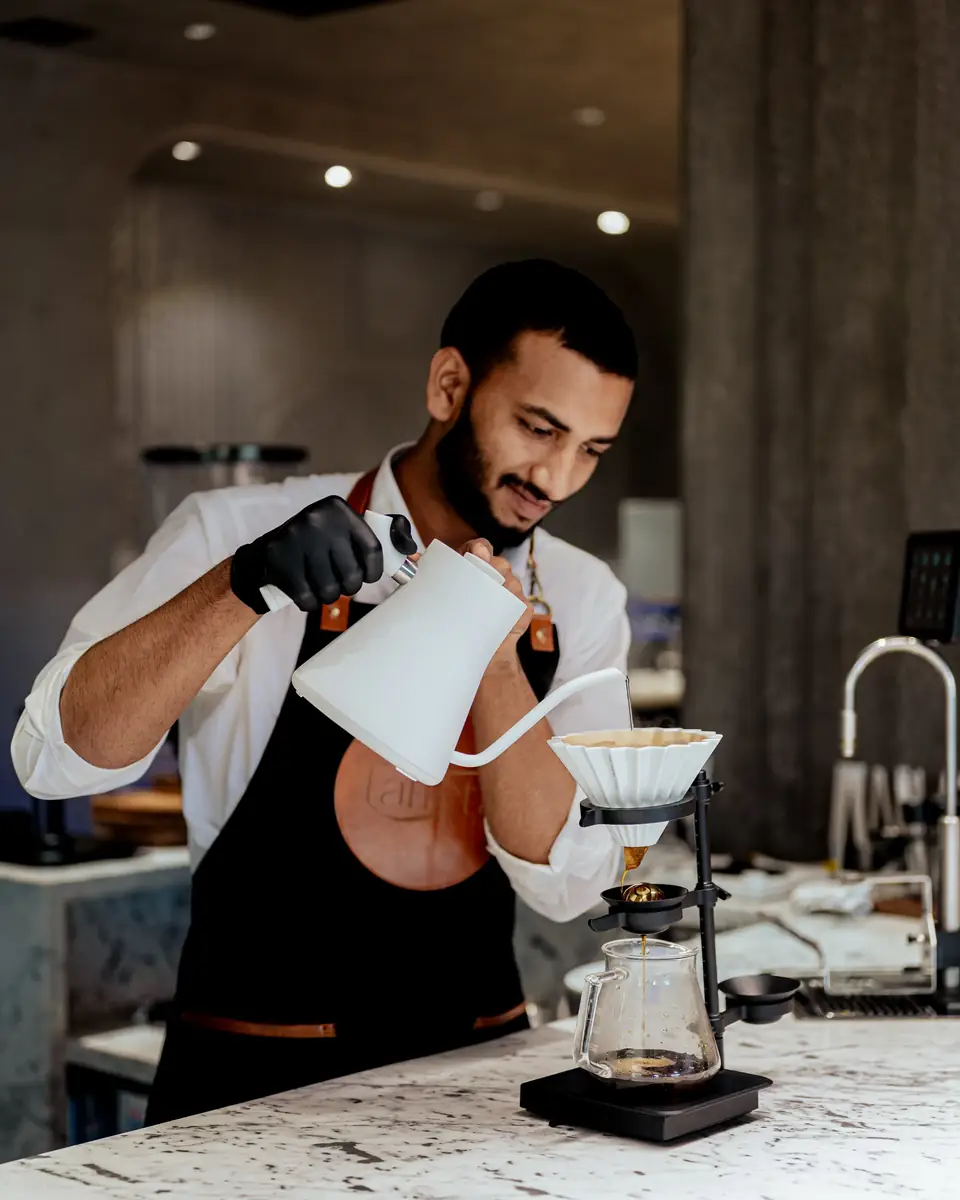 A barista pouring a slow pour-over from a white gooseneck kettle