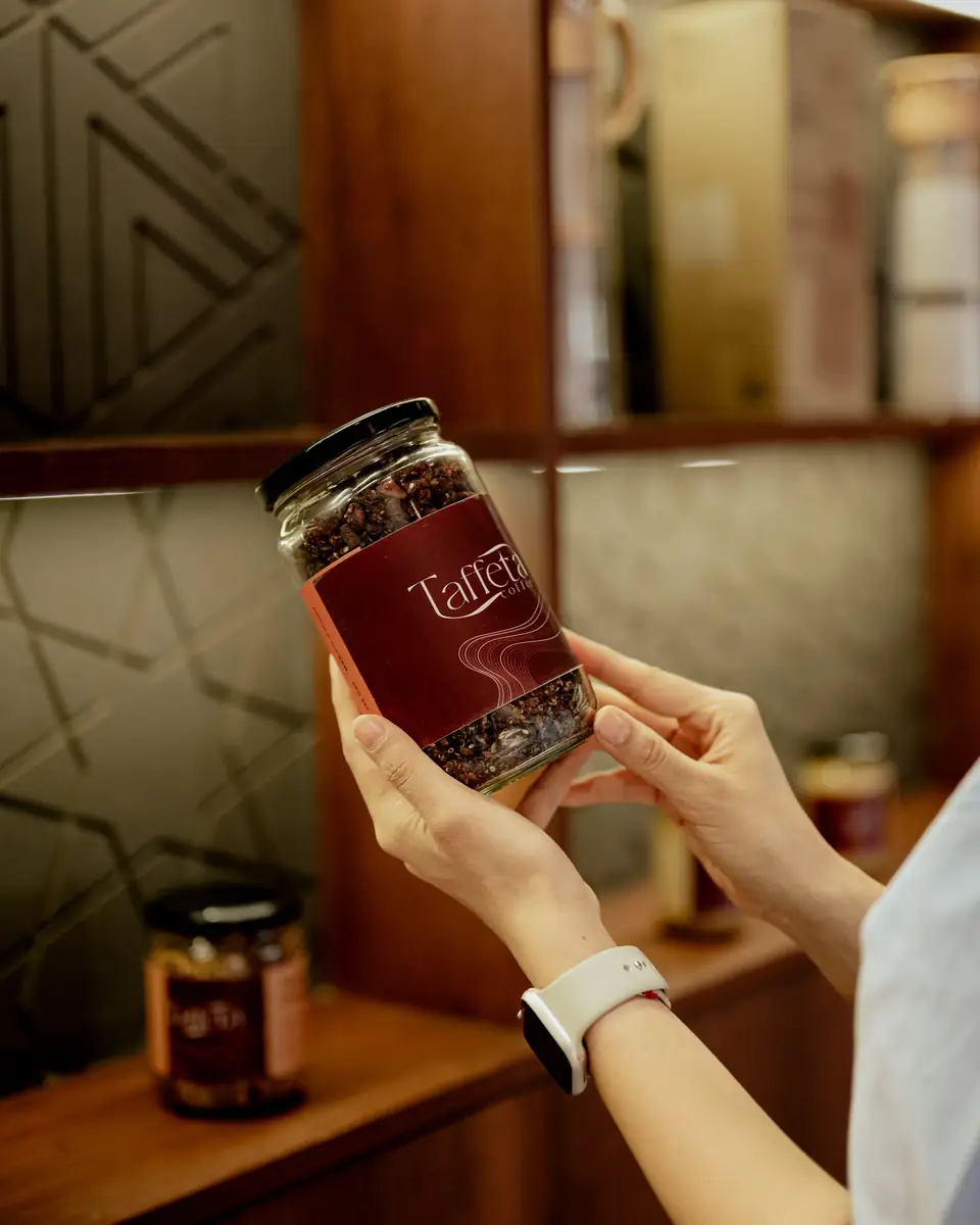 Hands holding up a jar of Taffeta coffee beans in front of the retail shelf