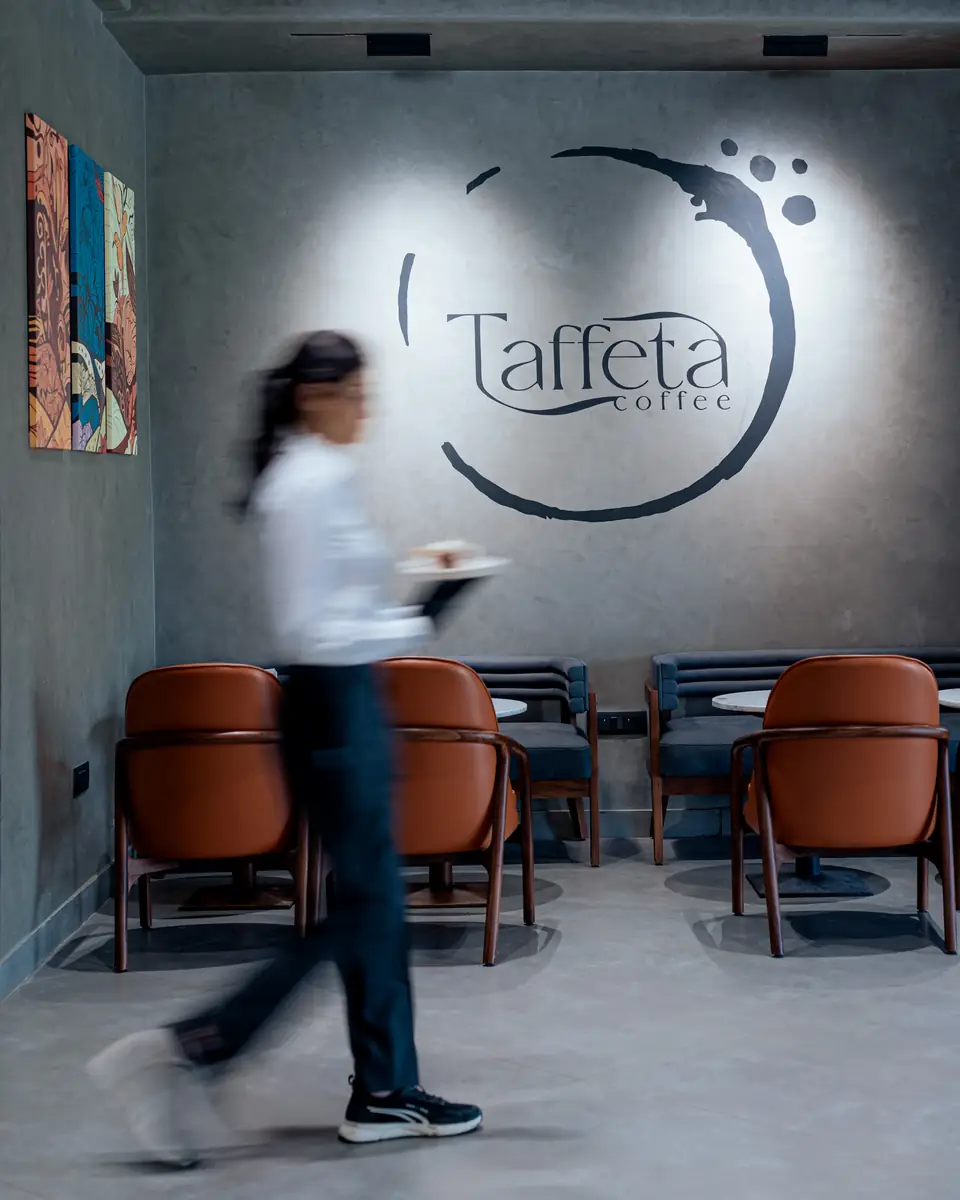 A server walking past the Taffeta logo wall carrying a cup