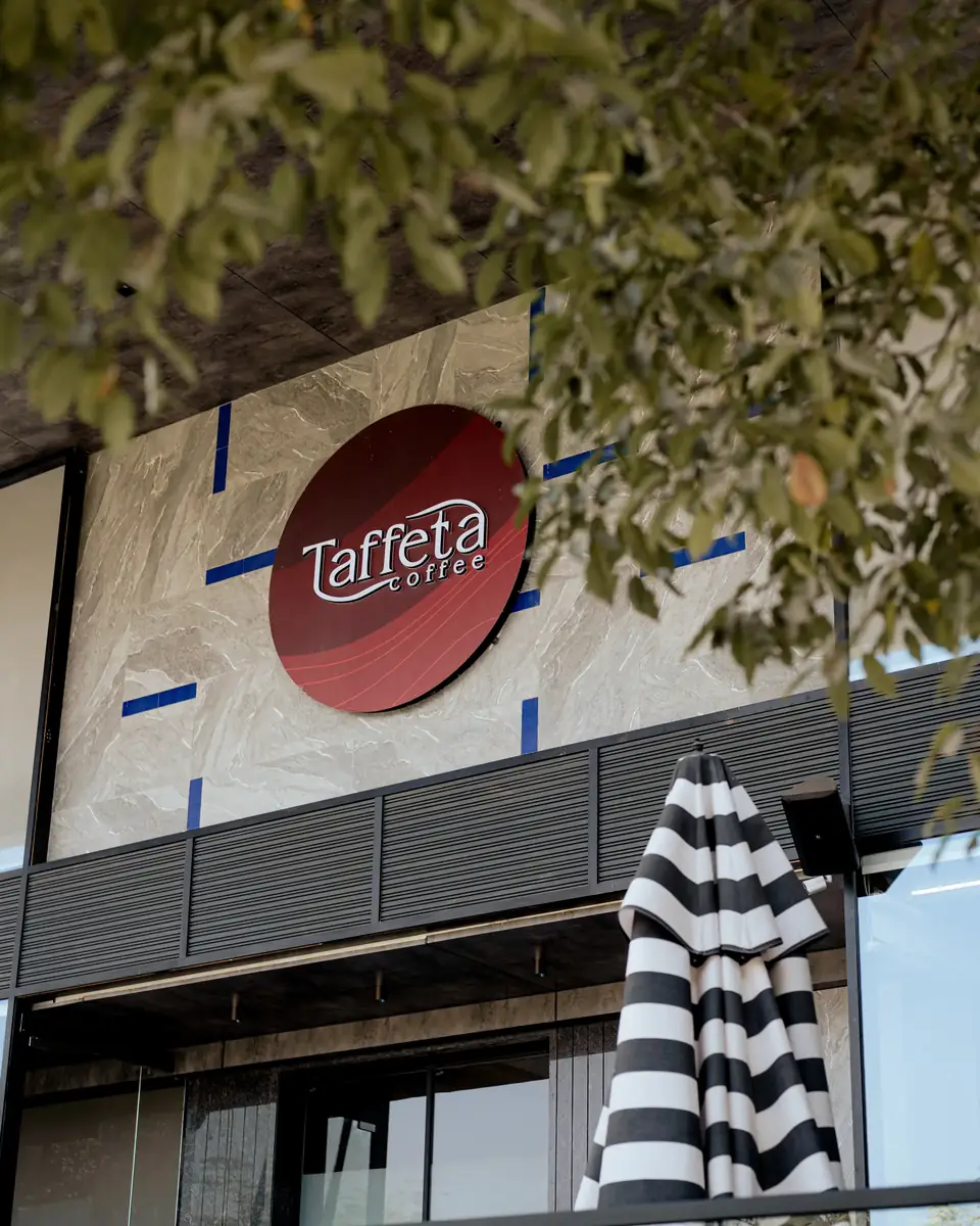The red Taffeta Coffee roundel sign on the marble façade, framed by leaves