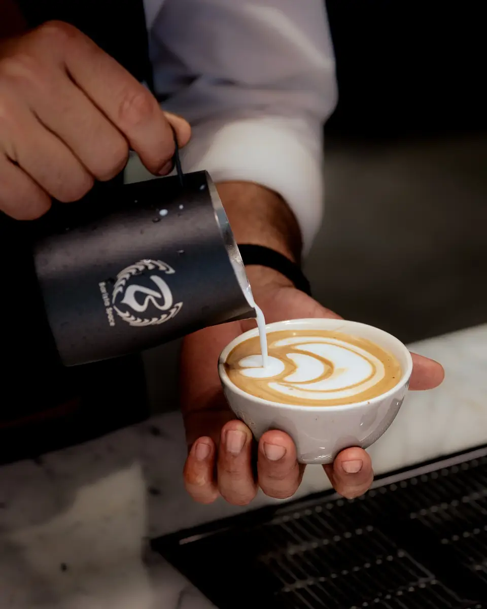 A barista pouring a rosetta of latte art into a white cup