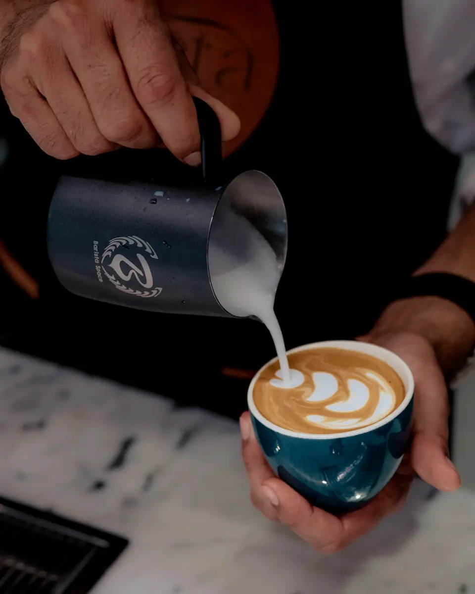 Milk pouring into a teal cup to start a latte art pattern