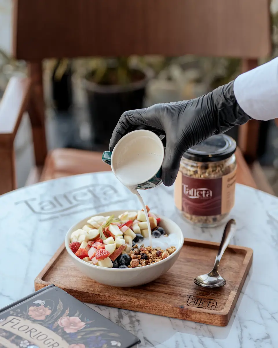 Milk poured over a fruit and granola bowl on a wooden Taffeta tray