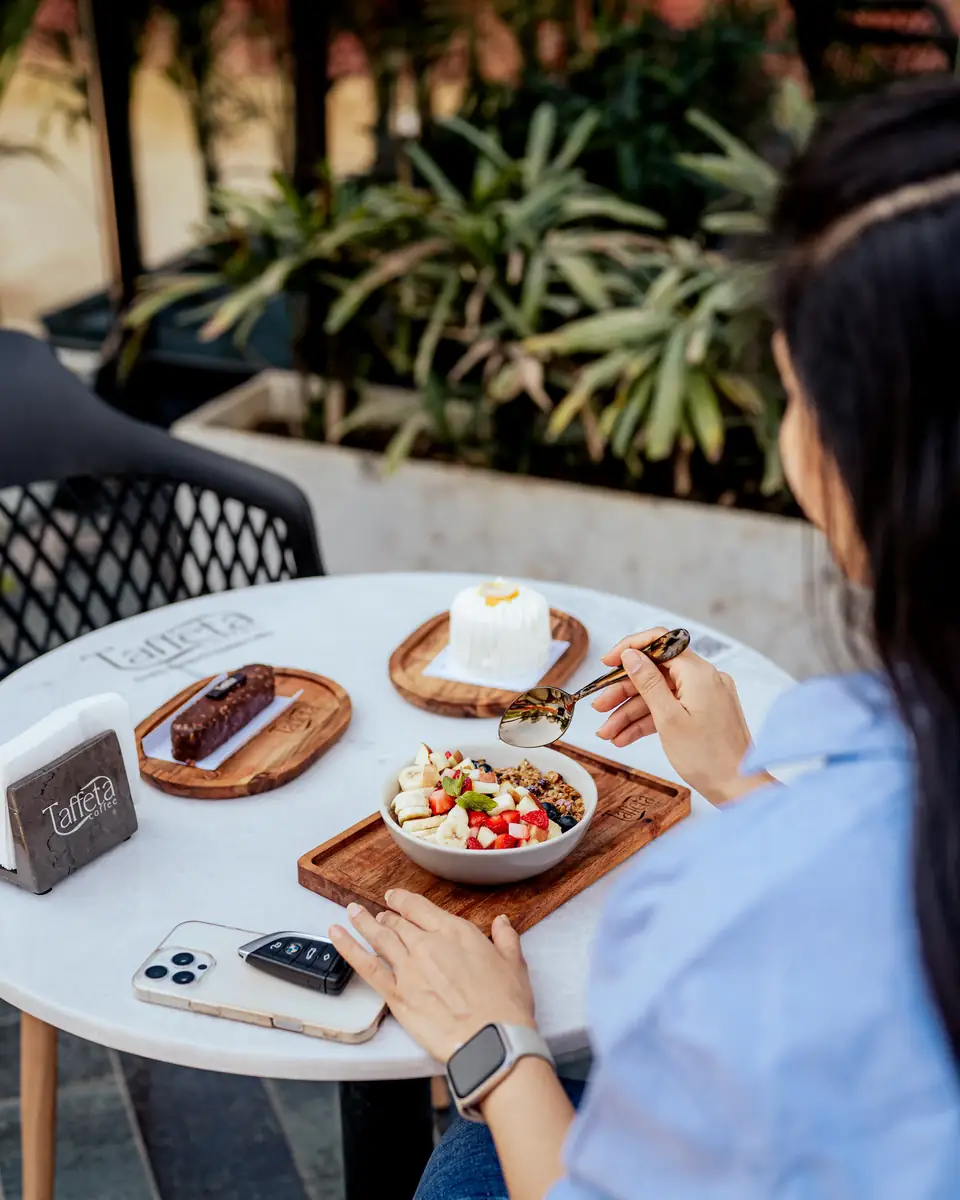 A guest at a terrace table set with desserts, a fruit bowl and a phone