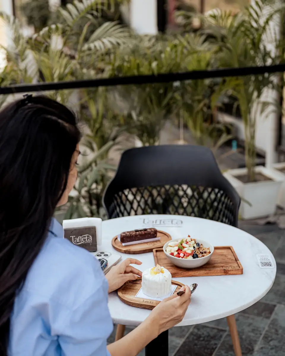 A guest sitting at a terrace table among palms with desserts and a fruit bowl