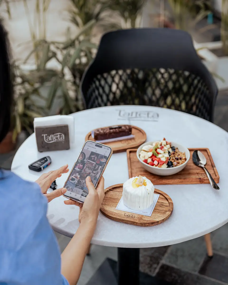 A guest scrolling a phone over desserts and a fruit bowl on the terrace