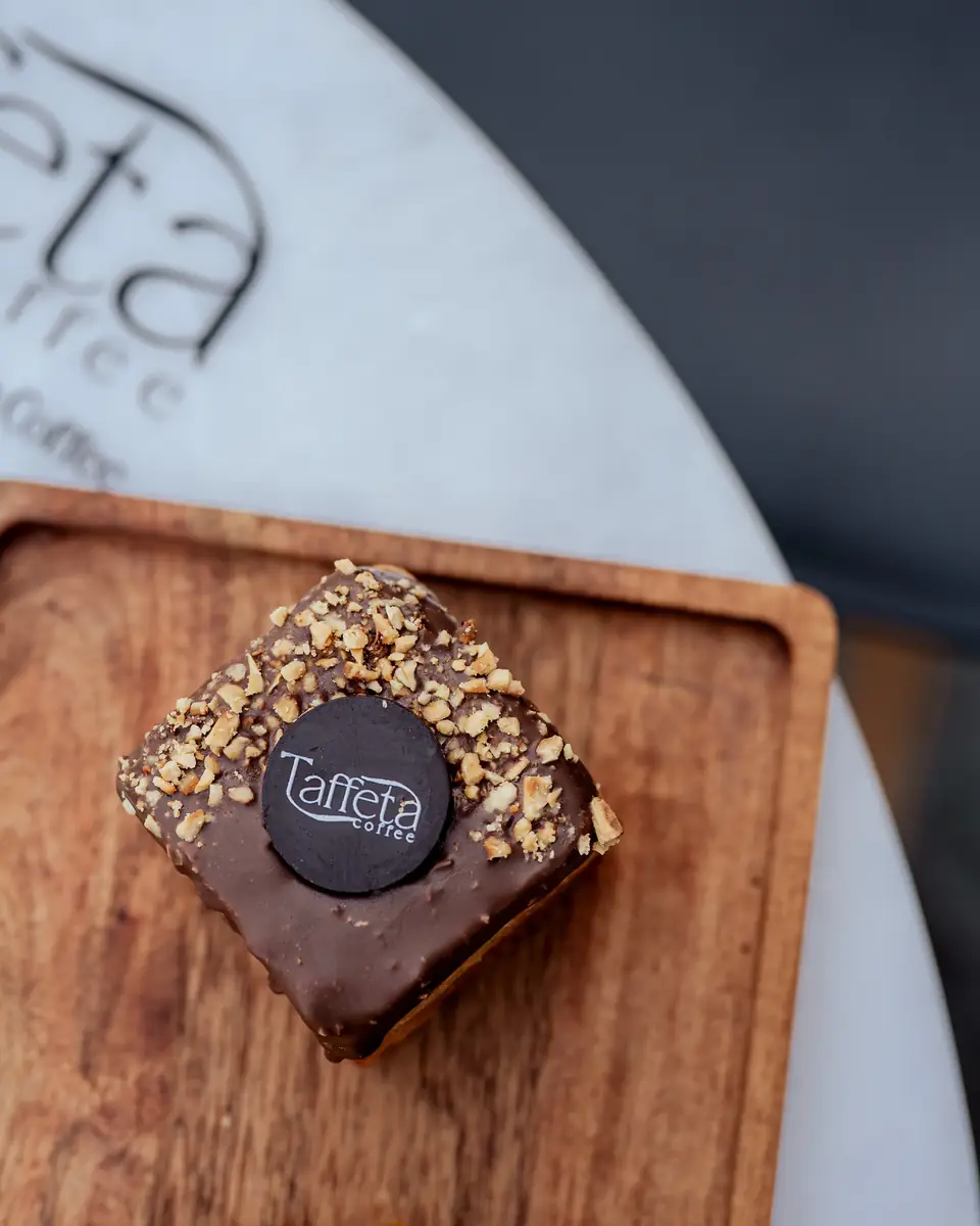 A nut-topped chocolate square on a wooden board on a marble table