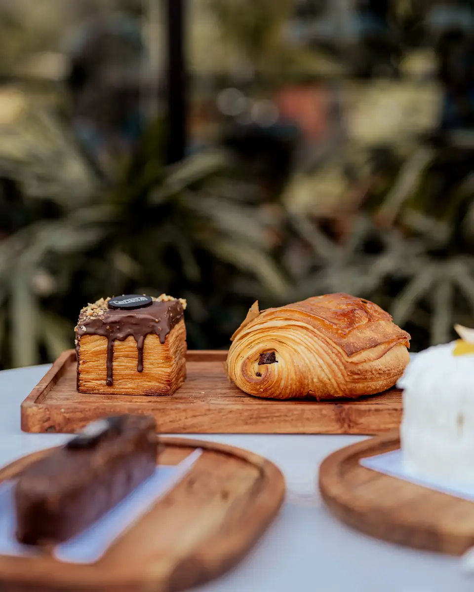 A chocolate pastry and a pain au chocolat on a board, with palms behind