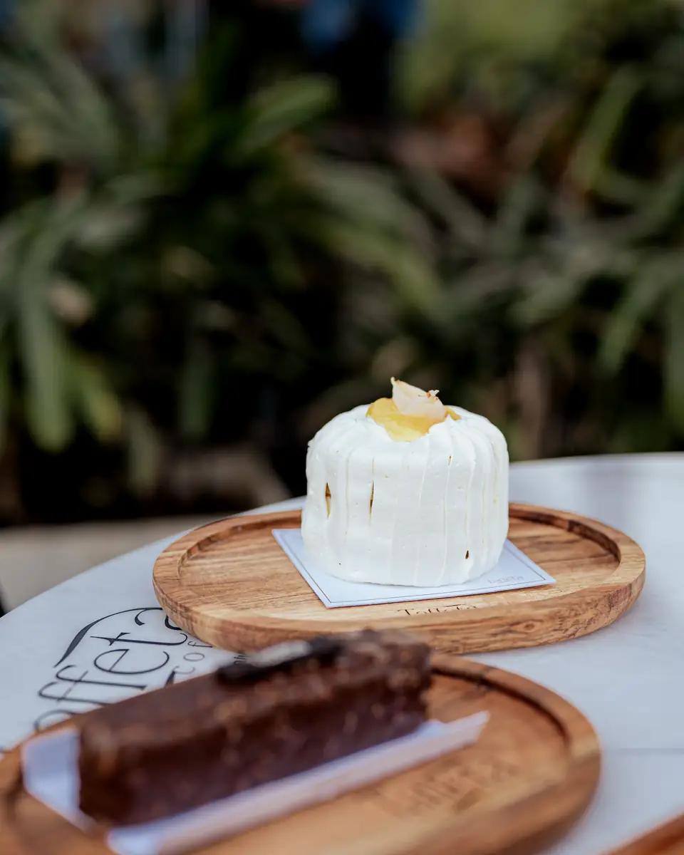 A white frosted cake and a chocolate slice on wooden boards on the terrace