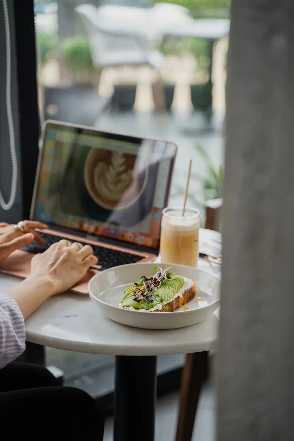 A guest working on a laptop beside a latte and a plated toast